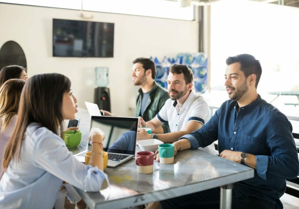Team of people gathered around a conference table with laptops and coffee mugs